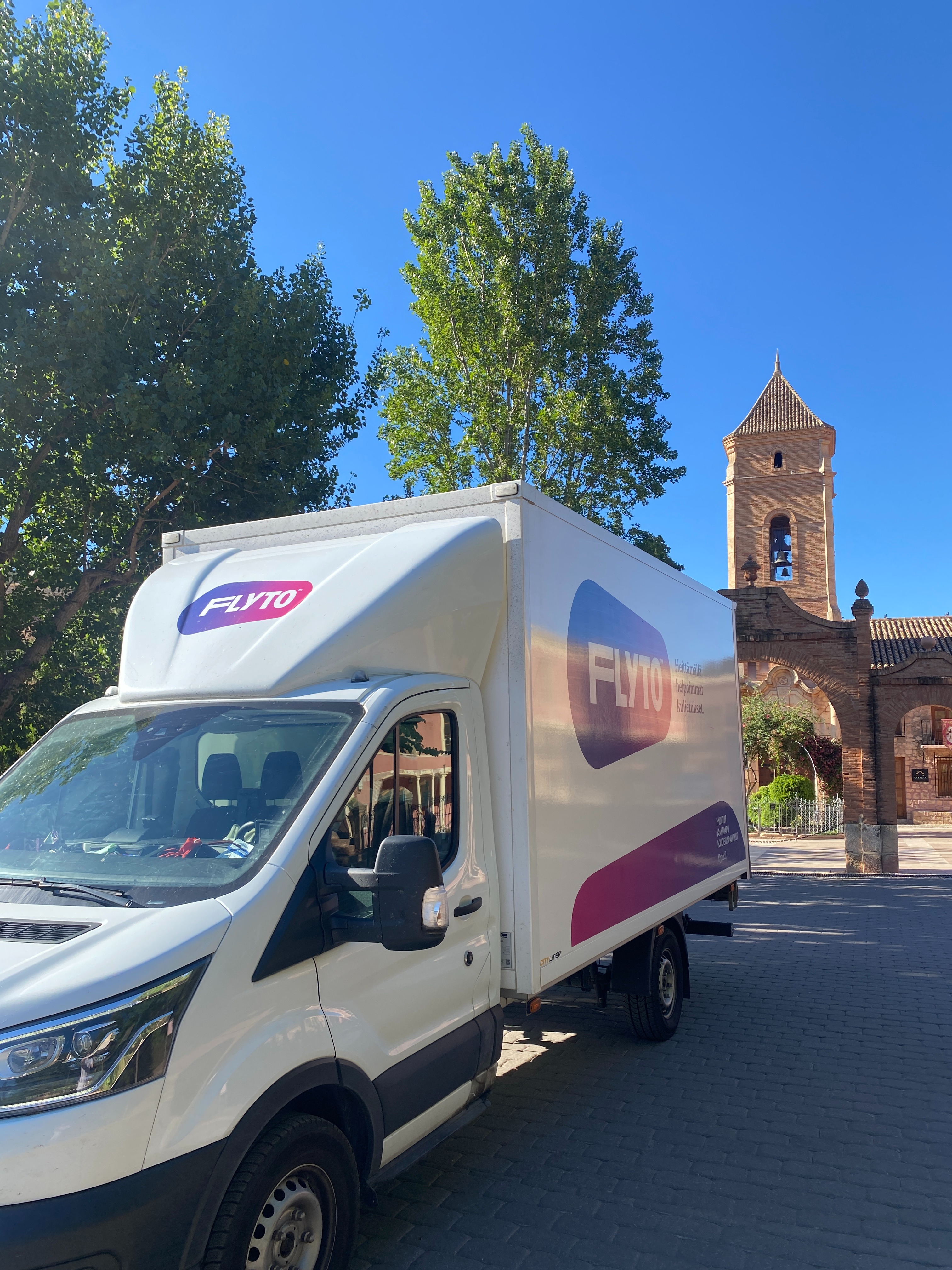 FLYTO moving truck parked near historic church with bell tower in European city