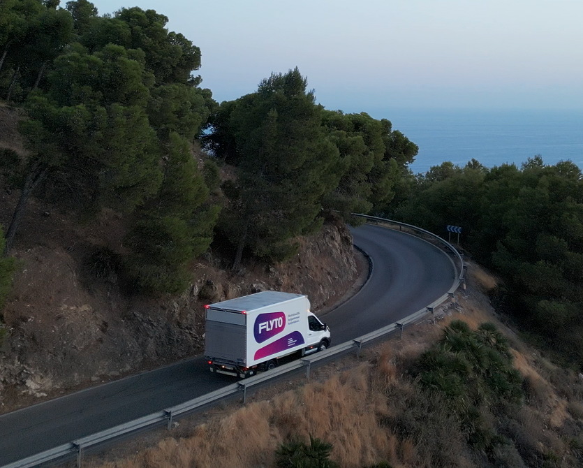 FUTO moving truck on winding coastal mountain road surrounded by green forest and sea views