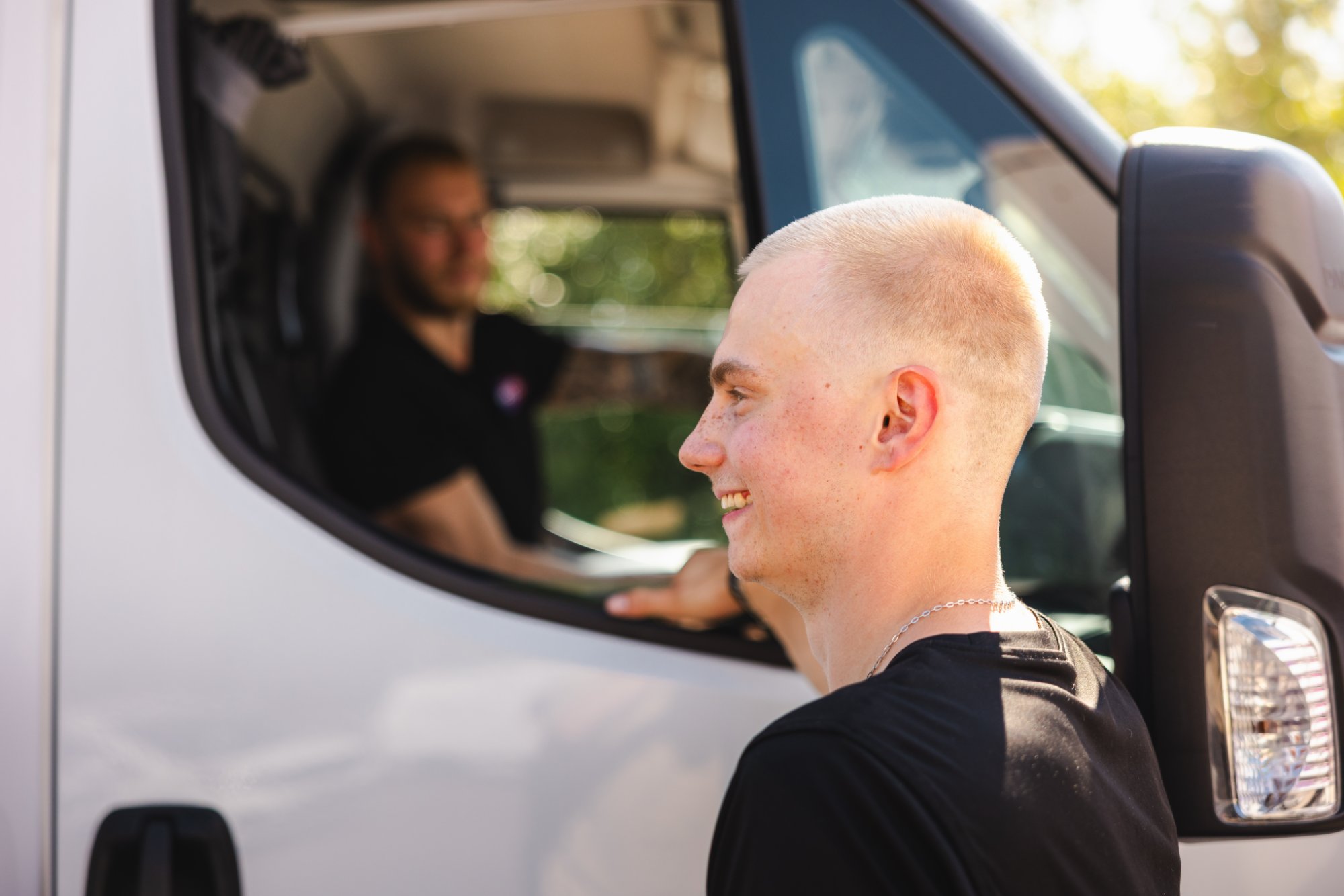 Smiling moving company worker beside white van talking with colleague in driver seat
