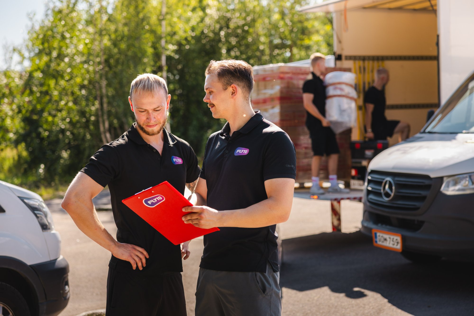 Moving company workers reviewing checklist during relocation service with truck being loaded in background