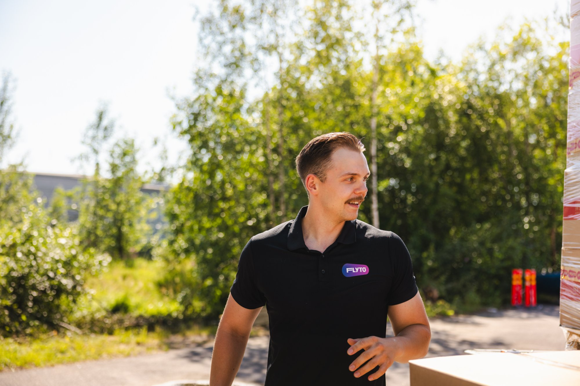 FLYTO moving company employee in black polo shirt standing outdoors near moving boxes