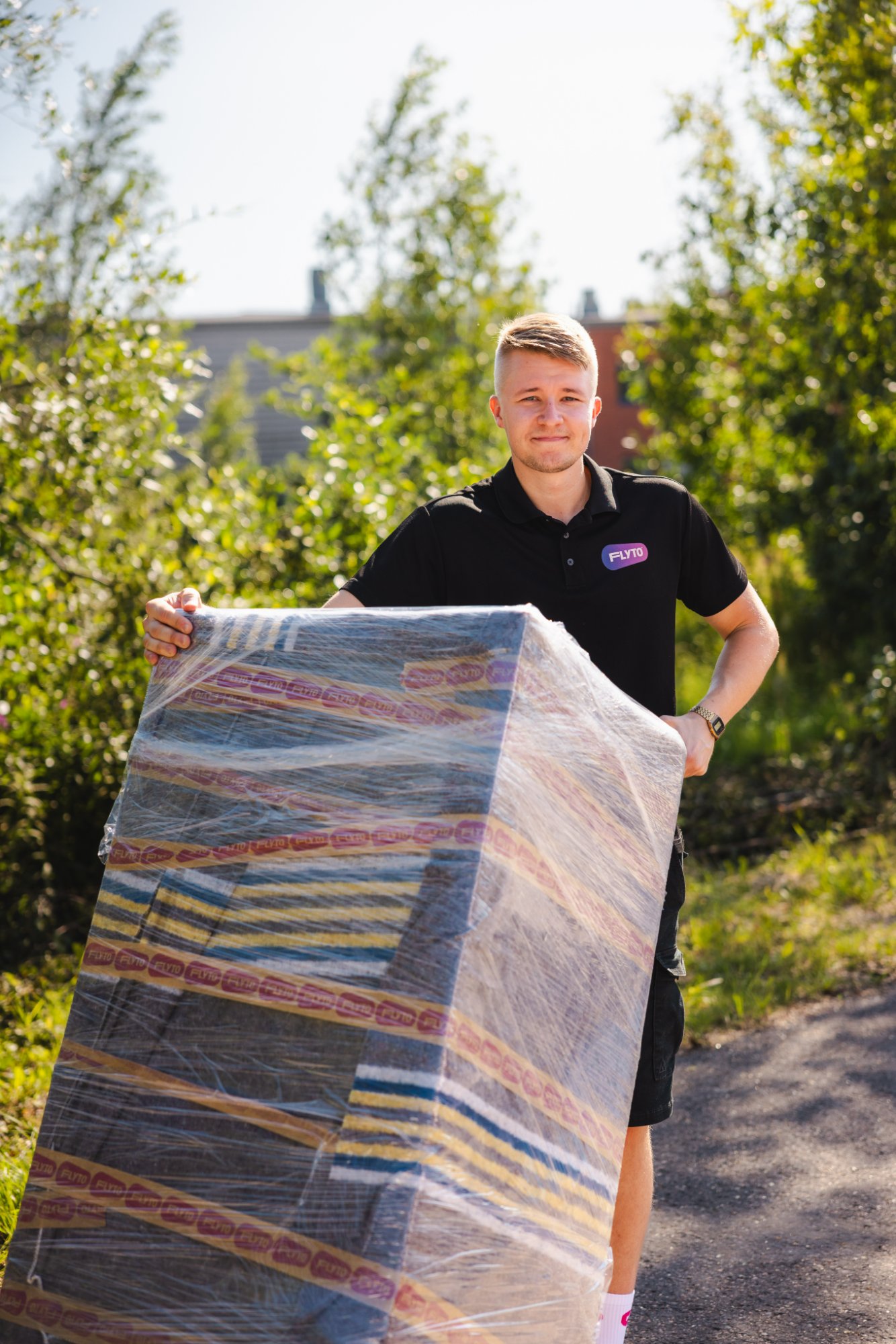 Moving company worker carrying wrapped mattress outdoors on sunny day