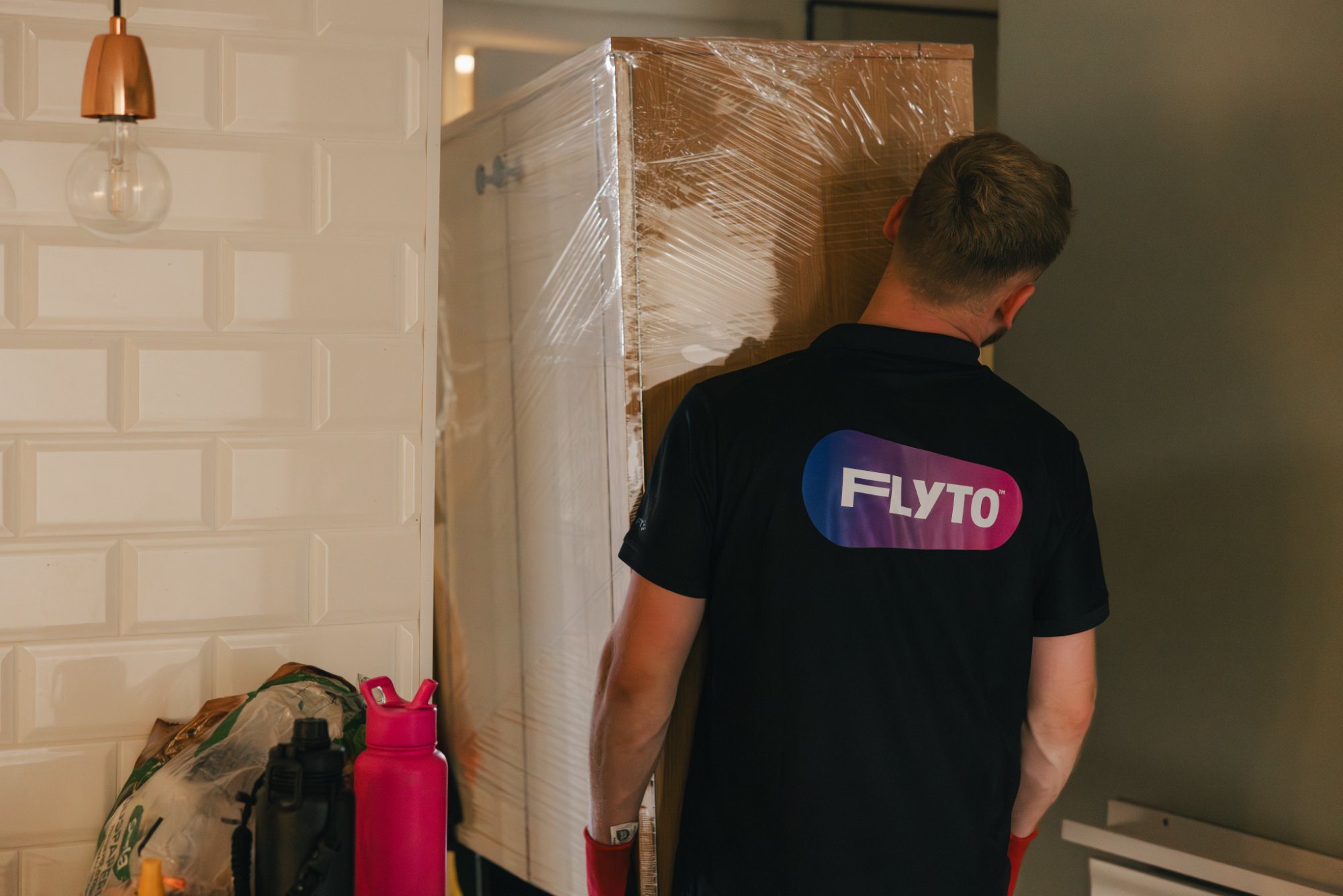 FLYTO moving company worker transporting wrapped furniture through home interior