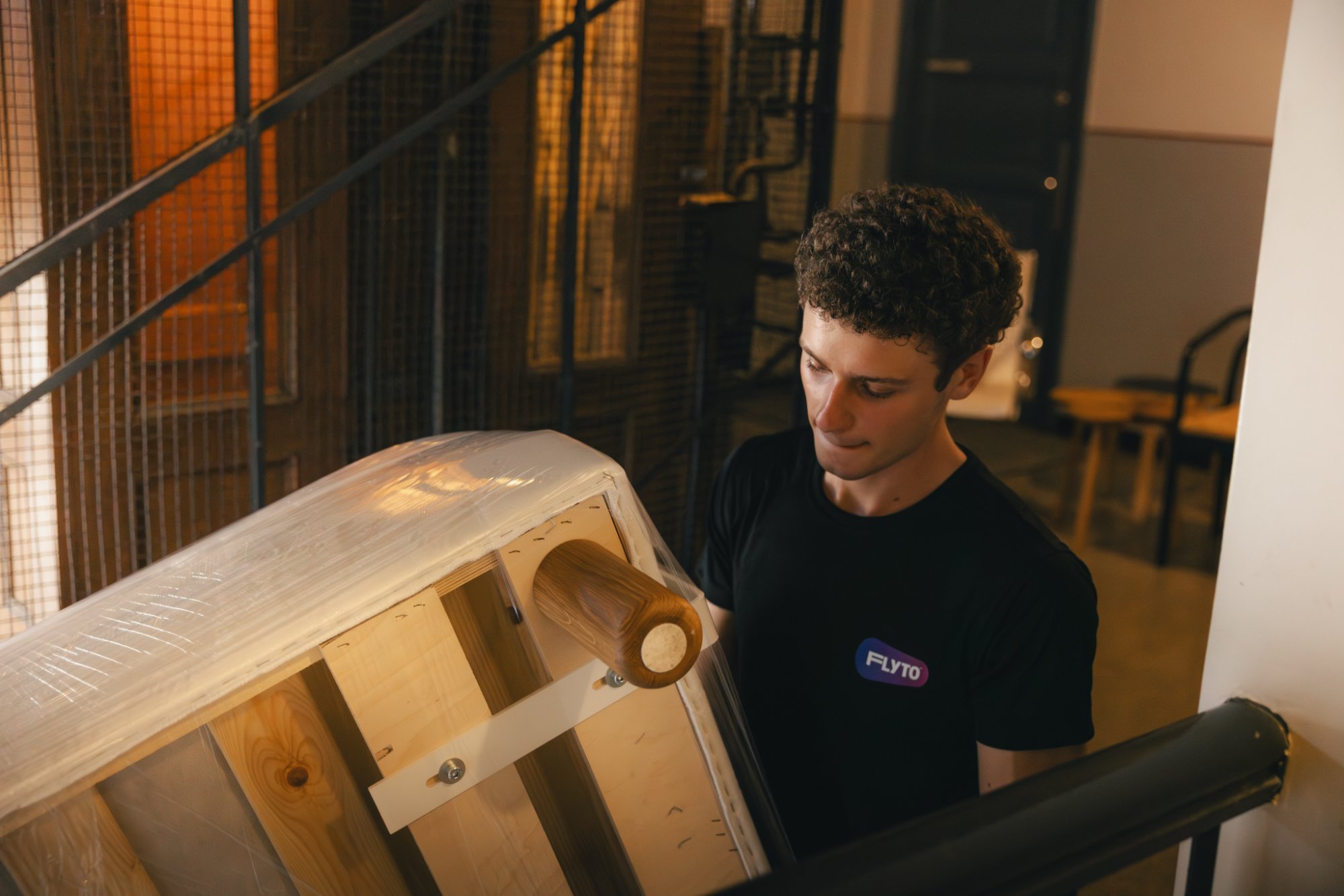 Moving company worker wrapping wooden barrel with protective film on staircase