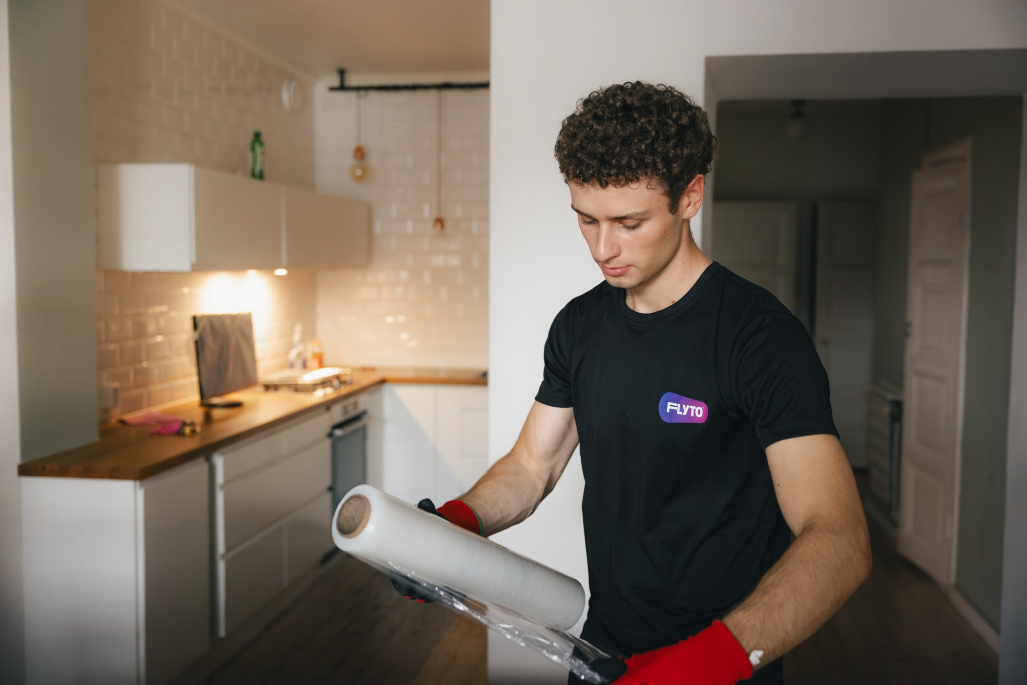 Professional mover wrapping items with protective material in modern kitchen during relocation service