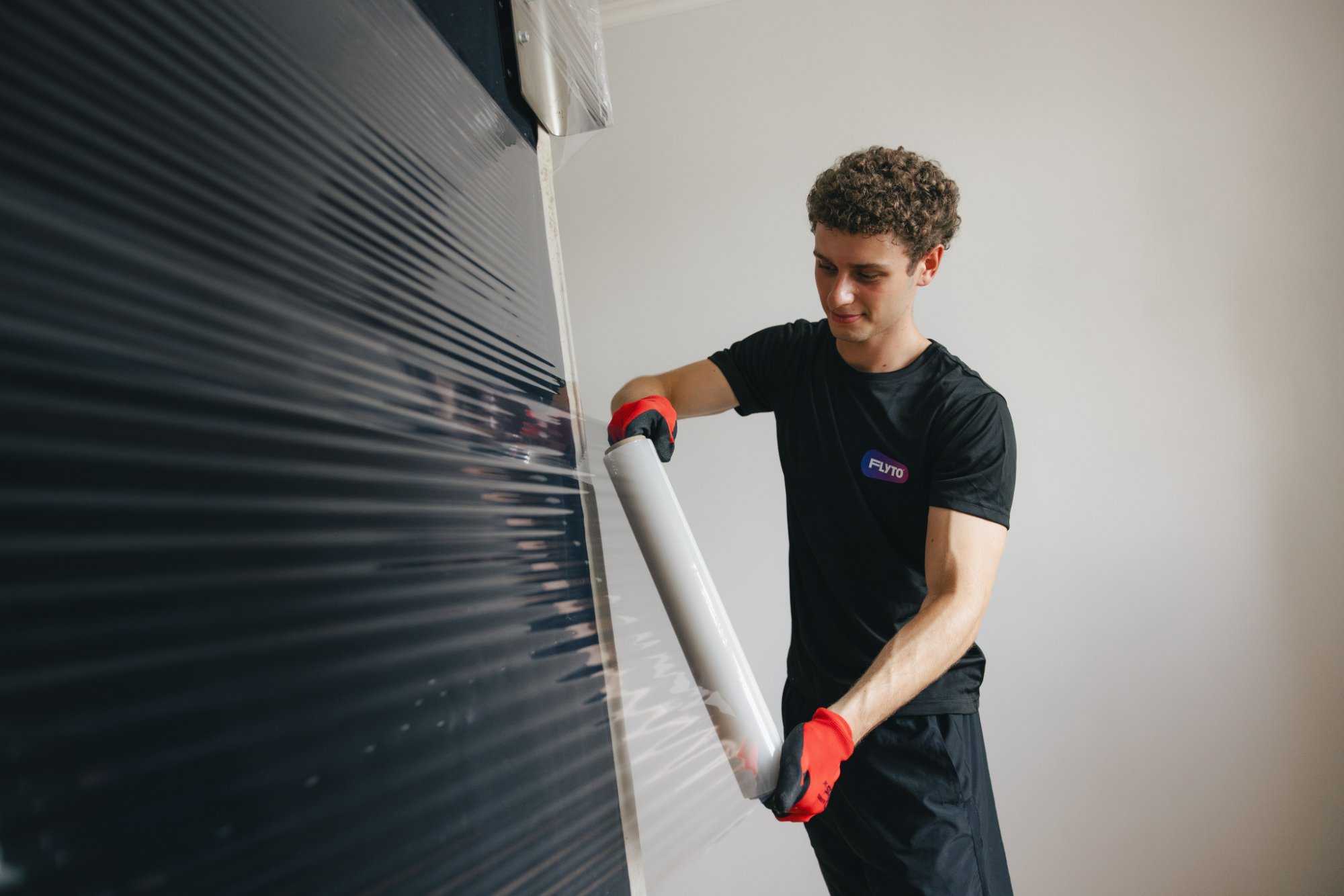 Moving company worker wrapping furniture with protective plastic film wearing gloves