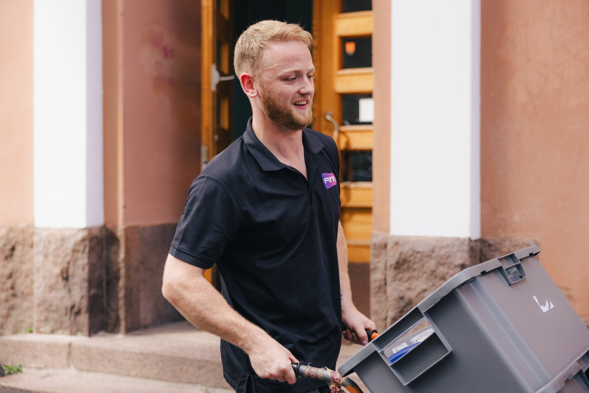 Professional mover carrying plastic moving box in front of residential building