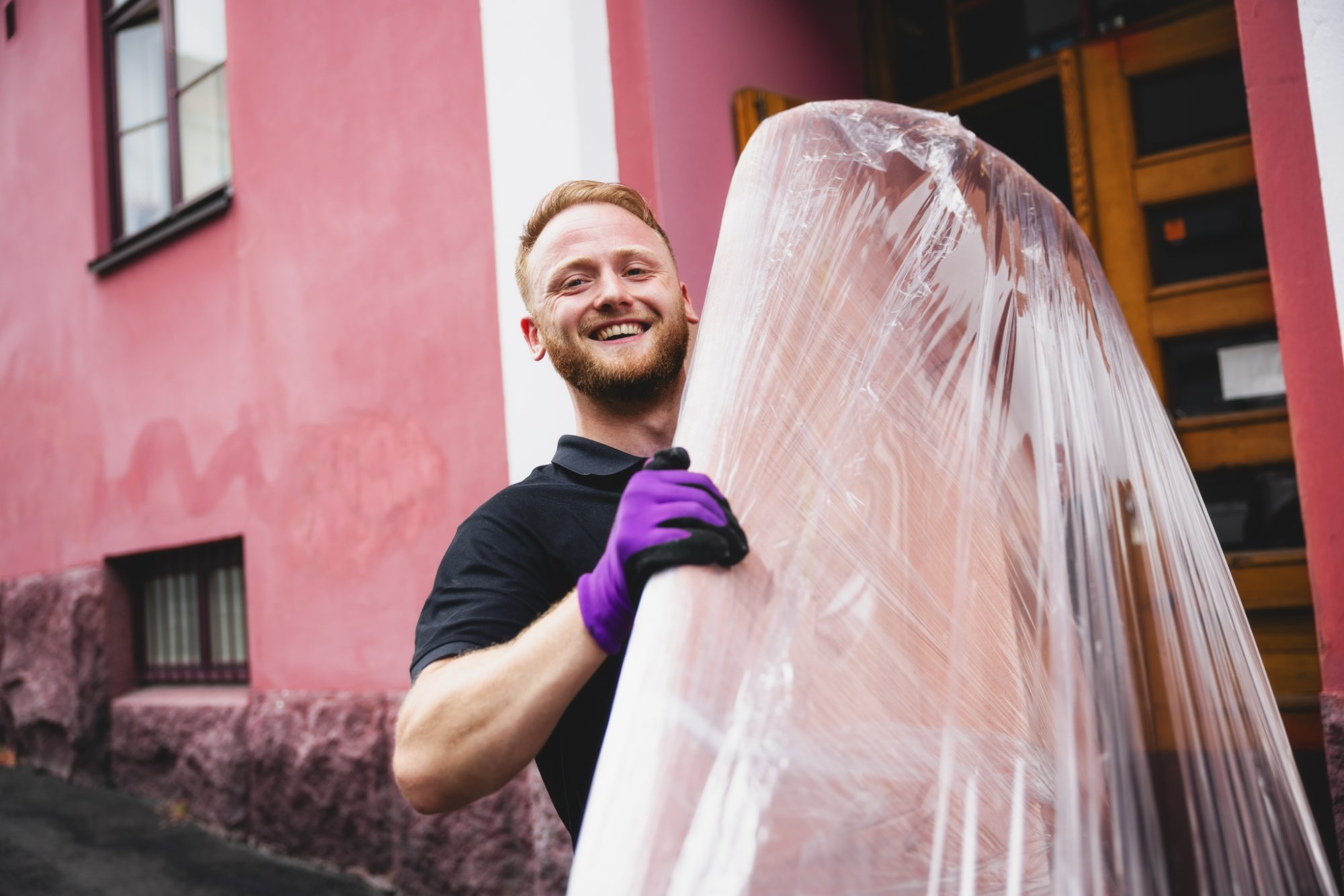 Professional mover carrying wrapped furniture in front of pink building