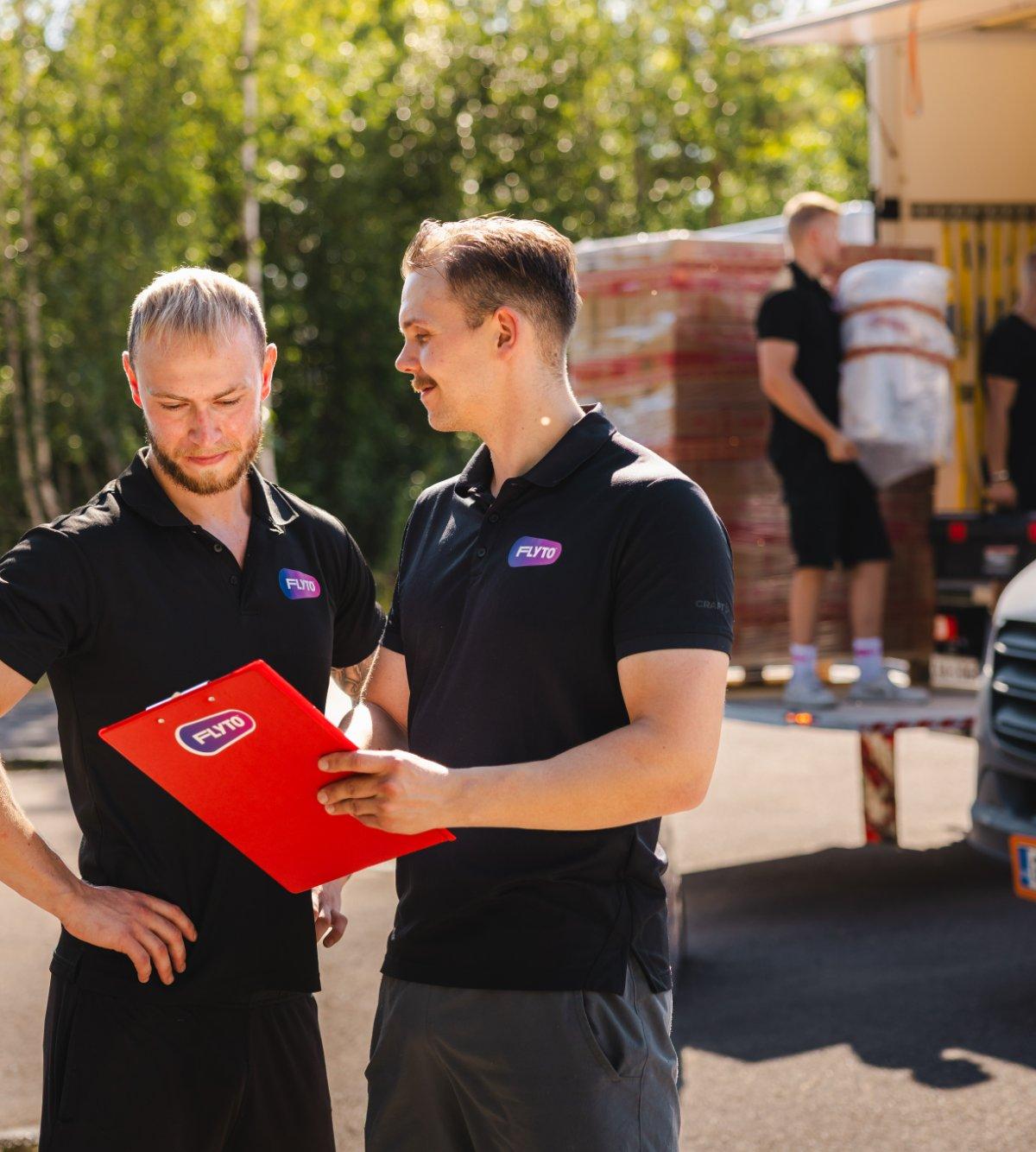 Moving company workers reviewing checklist during relocation service with truck being loaded in background