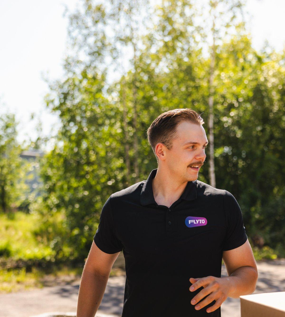 FLYTO moving company employee in black polo shirt standing outdoors near moving boxes