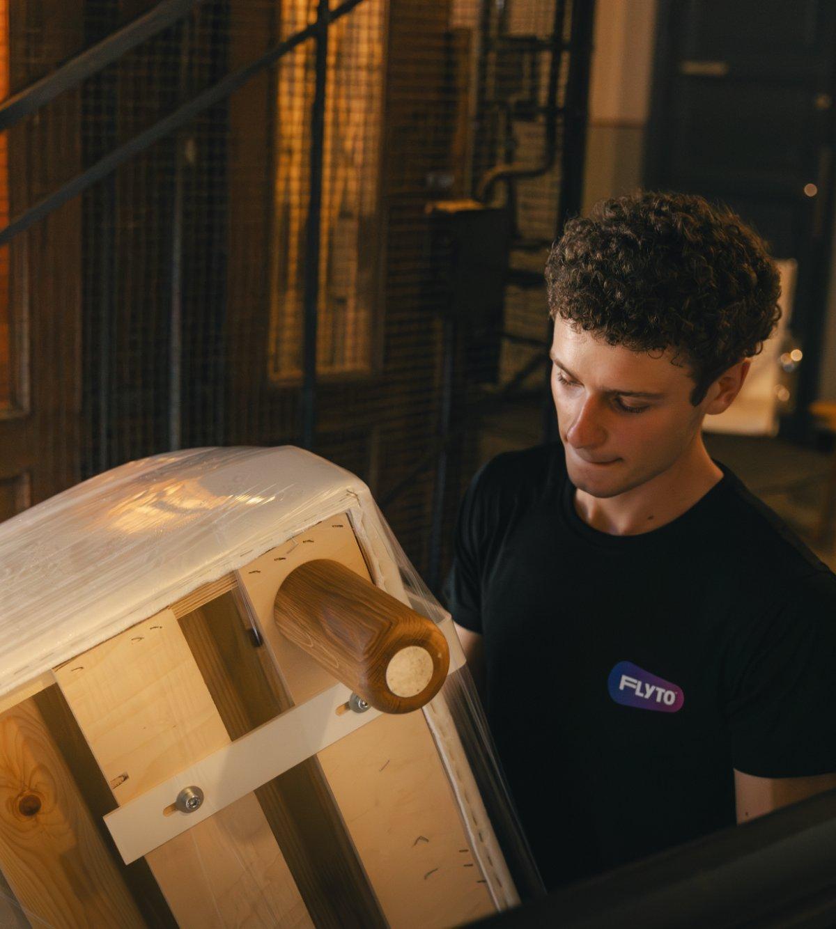 Moving company worker wrapping wooden barrel with protective film on staircase