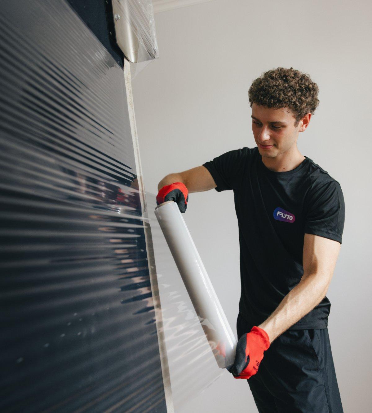 Moving company worker wrapping furniture with protective plastic film wearing gloves